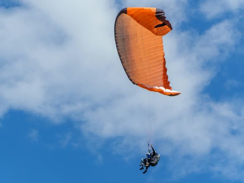A tandem paraglider in flight against a wide blue, cloudy sky.